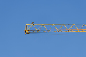 Yellow construction crane boom extending across clear blue sky © ANTONIO COSTA
