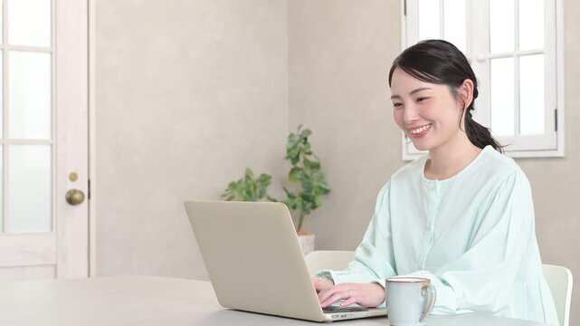 観葉植物のあるリビングでノートパソコンを使いながら笑顔を見せる日本人女性