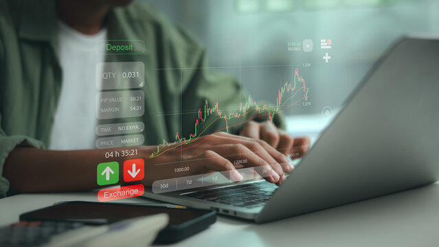 Close up of trader analyzing stock market chart and executing exchange order on laptop keyboard, with virtual trading interface graphics on desk in office.