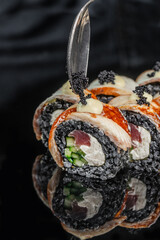 Close up of decorated sushi rolls with fish, cucumber, creamy filling, orange topping, black sesame pearls, and spoon against dark background food arrangement © Надія Коваль
