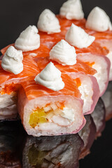 Closeup sushi roll topped with salmon slices and white cream rosettes, revealing rice, seafood, and colorful filling against a dark reflective surface © Надія Коваль
