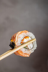 Closeup sushi roll with salmon, rice, sesame coating, creamy filling, and wooden chopsticks against a neutral background, Japanese cuisine food photograph © Надія Коваль