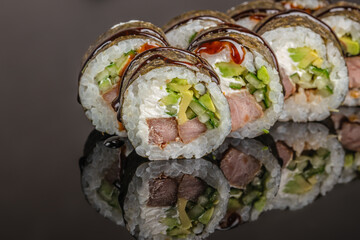 Sliced sushi rolls with rice, seaweed, avocado, cucumber, and fish arranged on a reflective black surface in close-up food photography composition © Надія Коваль