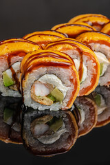 Glossy sushi rolls with orange sauce, rice, seafood, avocado, and seaweed arranged in a close up row on a reflective black surface, Japanese cuisine © Надія Коваль