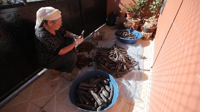 Senior woman peeling and preparing black carrots with knife on balcony for traditional fermented turnip juice salgam