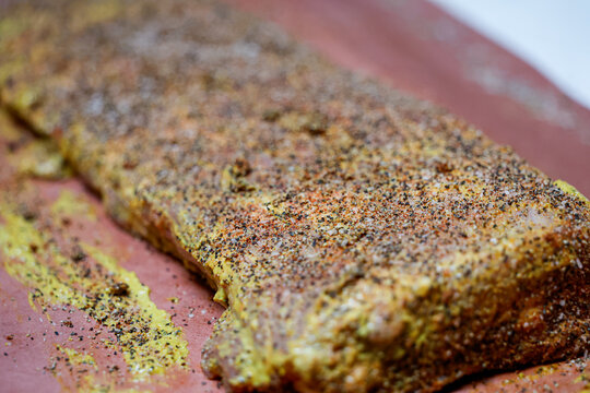 Barbecue pork ribs smothered in mustard, black pepper, salt, and garlic powder resting on butcher paper before going in the pellet grill smoker to cook.