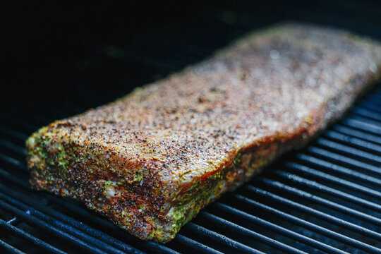 Barbecue pork ribs cooking on a smoker. The bbq meat is coated with mustard and seasoned with salt, black pepper, and garlic powder for a tasty crunchy bark. 