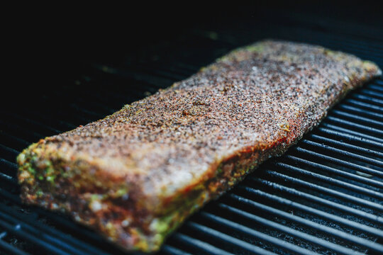 Barbecue pork ribs cooking on a smoker. The bbq meat is coated with mustard and seasoned with salt, black pepper, and garlic powder for a tasty crunchy bark. 