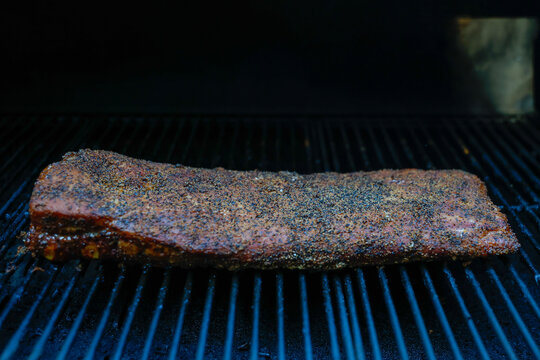 Barbecue pork ribs seasoned with salt, pepper, garlic for a crunchy bark. The bbq meat is cooking on a pellet grill smoker. 