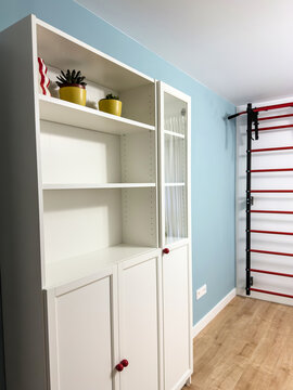White bookcase with glass door, red knobs and colorful decor against a light blue wall in a home office