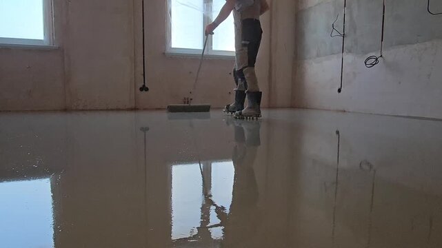 Close-up shot of self-leveling floor compound poured onto a surface and spreading out evenly. Construction worker leveling the floor. Liquid screed flows and fills the surface. Renovation and construc