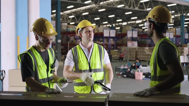 Team of White men warehouse workers in yellow helmets using tablets, working, talking, discussing, checking, and high fiving after loading cargo boxes into container at logistics distribution factory.