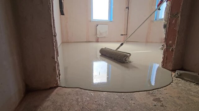 Close-up shot of self-leveling floor compound poured onto a surface and spreading out evenly. Construction worker leveling the floor. Liquid screed flows and fills the surface. Renovation and construc
