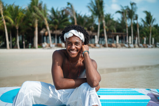Smiling happy young black man enjoys a sunny day paddling, surf on a tropical beach resort
