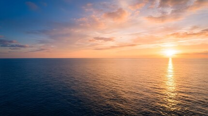Fototapeta premium Vast calm blue ocean water meeting pastel golden sunrise horizon with soft clouds and sunbeams reflecting on gentle sea ripples.