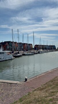 Scenic marina and harbor with moored sailboats and colorful traditional Dutch houses under a partly cloudy blue sky