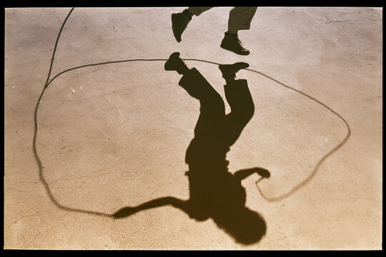 Minimalist jumping rope shadow with intense action low angle hard sunlight sepia