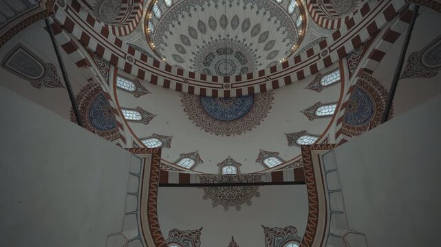 Low angle tilt up shot of magnificent interior dome with ornate Islamic calligraphy and Ottoman fresco art in historic mosque   