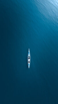 Minimalist lone kayak on calm lake with cold cyan blue lighting drone aerial