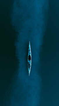 Minimalist lone kayak on calm lake with cold cyan blue lighting drone aerial