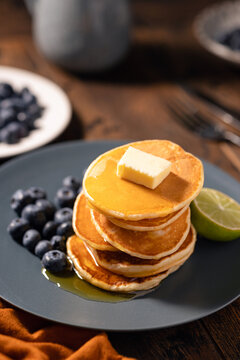 Stack of pancakes with blueberries on white plate served with cup of black coffee. Wooden table background