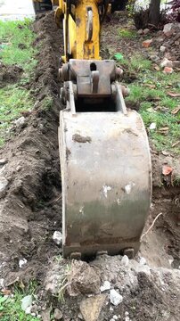 Close up of an excavator bucket scooping dirt while digging a trench, heavy machinery work, construction site.