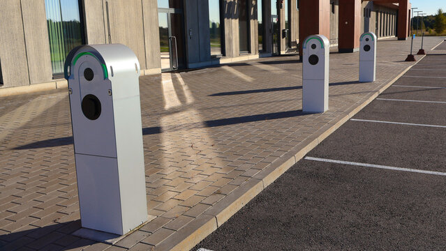 Electric car charging stations standing in a modern office building parking lot during a sunny day, representing sustainable energy, green technology, and the future of transportation
