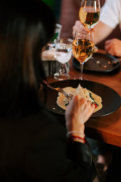 Woman eating delicious pasta at a restaurant table while sharing wine with her companion at dinner