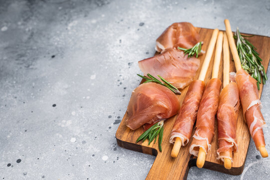 Prosciutto-wrapped grissini and a bowl of marinated olives on a textured gray background. Classic Mediterranean snack.
