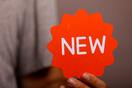 A person displays a bright orange star-shaped tag with the word NEW, symbolizing innovation.
