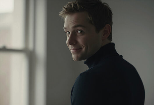 Charming young man turning around looking at camera with playful smile near window