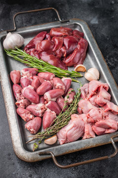 Assorted raw poultry giblets including chicken liver, gizzards, and hearts with herbs and garlic on rustic metal tray top view.