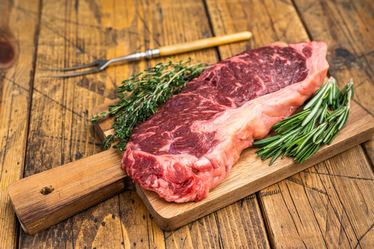 Uncooked sirloin steak with herbs on rustic wood excellent for gourmet cuisine barbecue concepts butcher promos and kitchen preparation scenes.