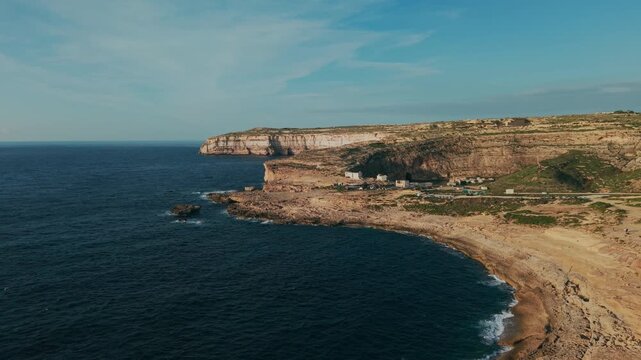 Aerial landscape of Dwejra on Gozo, Malta. Curved rocky bay, limestone coastline, cliffs and small buildings by the deep blue Mediterranean Sea.