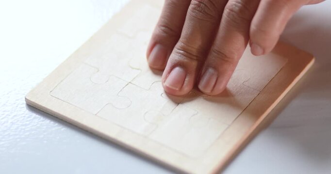 Hand placing a wooden jigsaw puzzle piece on a board, problem solving, solutions, strategy, logical thinking, concentration and completion