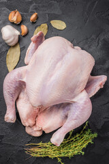 Raw whole chicken with fresh thyme and garlic cloves on a dark, black textured stone background. Preparing to cook poultry. © Mironov