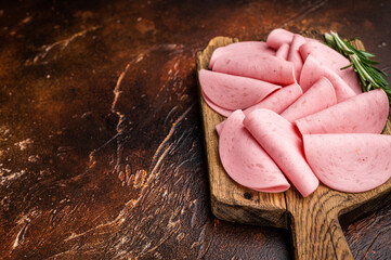 Heap of processed luncheon meat slices (salami) on a wooden board with herbs and pink rock salt. Dark, rustic food photography. © Mironov