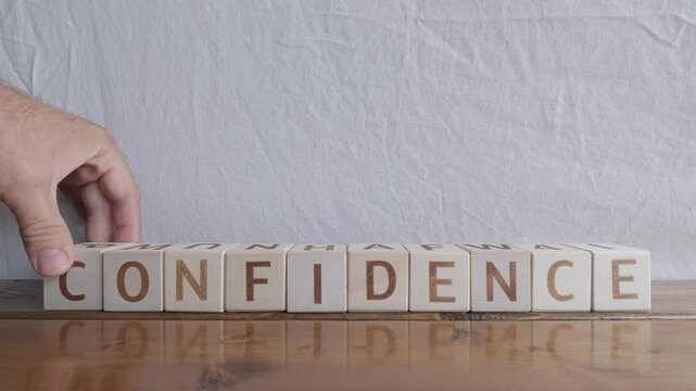 motivational word Confidence, laying out by hand from letters on wooden cubes, slow motion

