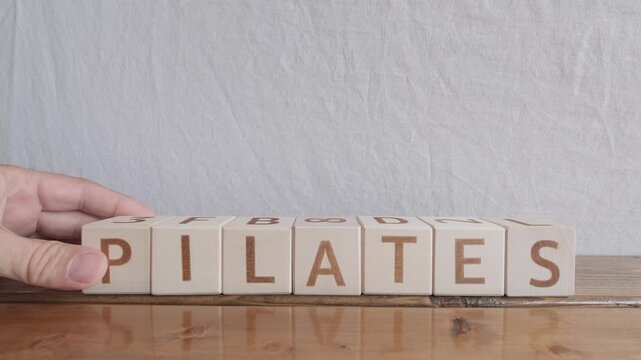 motivational word Pilates, laying out by hand from letters on wooden cubes, slow motion
