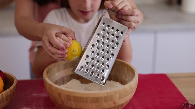 Detail of mother and daughter using grater while adding lemon zest into a cookie dough
