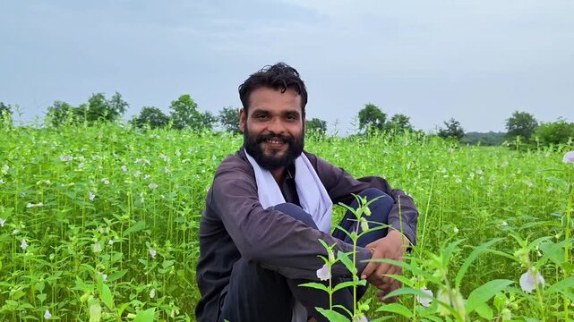 Happy indian farmer sitting and smiling in sesame crop field