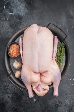 Uncooked duck carcass arranged with herbs and salt in rustic pan against textured dark surface ideal for culinary food photography.