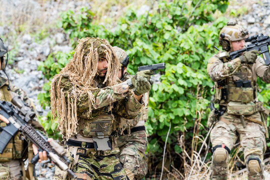 Soldiers participate in a training exercise using weapons and camouflage in a forested environment