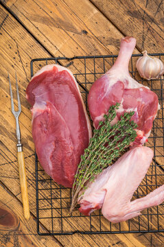 Raw duck breast thigh and wing on metal rack with vintage fork over rustic wooden background ideal for gourmet poultry.