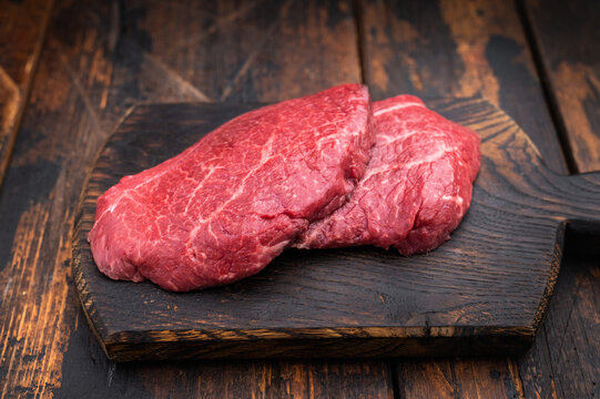 Uncooked Wagyu chuck steak with deep texture placed on rustic board with herbs and garlic over weathered timber surface perfect for butcher content.