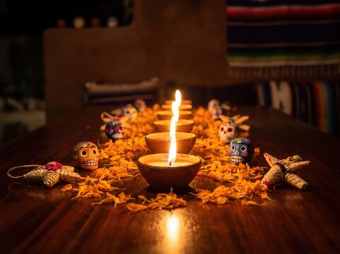 Candles lit on wooden table surrounded by marigold petals and colorful sugar skulls for day of the dead celebration