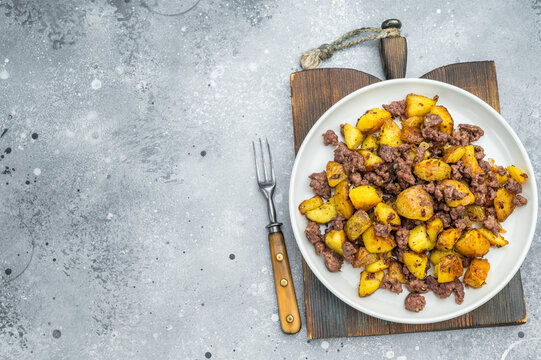 Crispy fried potatoes with ground beef served on a white plate, hearty homemade hash on a rustic grey background.