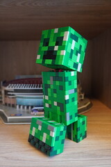 Fototapeta premium A green blocky Creeper character figure built from plastic construction bricks on a wooden shelf