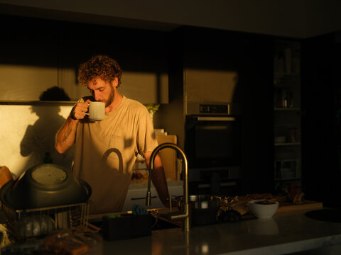 Man drinks from a mug on the kitchen at golden hour