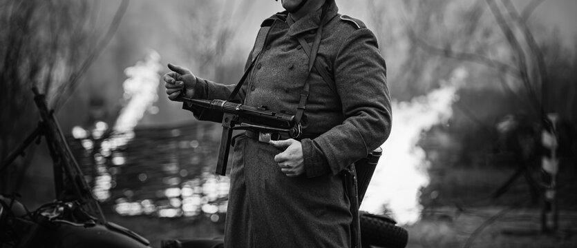 German Wehrmacht Infantry Soldier In World War Ii Standing Against The Background Of A Burning House. German WWII Soldier